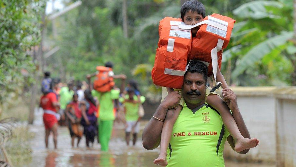 A fire & rescue worker carries a child on his shoulders away from the flood area