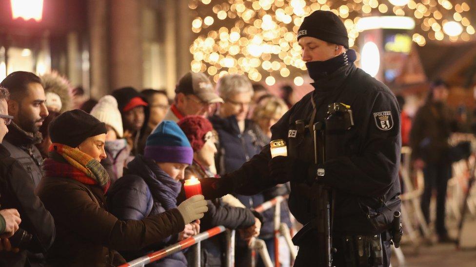 A policeman takes a candle from a mourner to place it at a makeshift memorial in Berlin