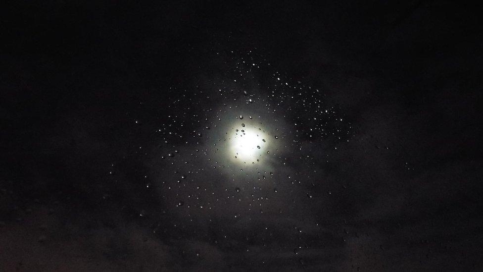 Moon seen through drops of water on a window pane