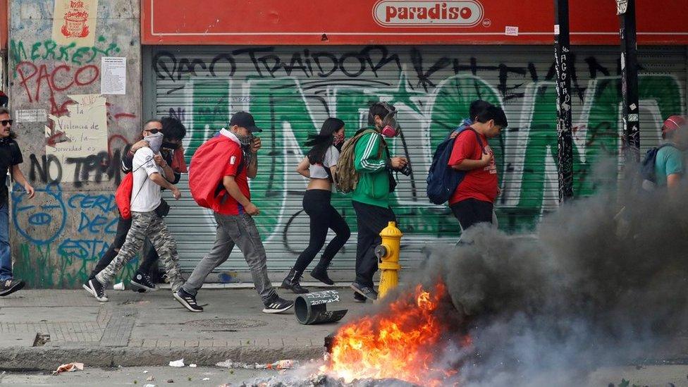 Protesters walk quickly past burning debris on the streets of Santiago