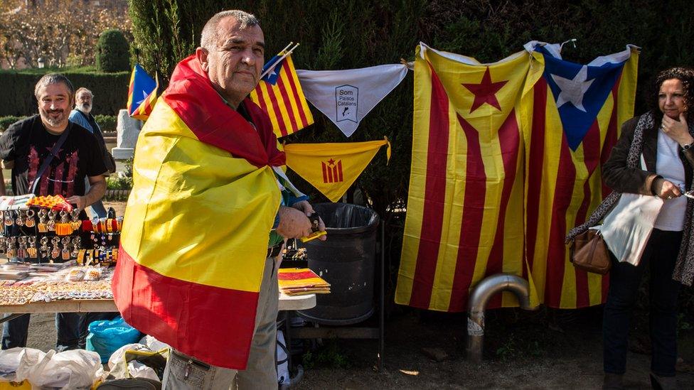 A man draped in a Spanish flag walks past a pro-independence souvenir stall outside the Catalan parliament