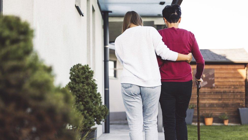 A female caregiver helps an elderly woman walk