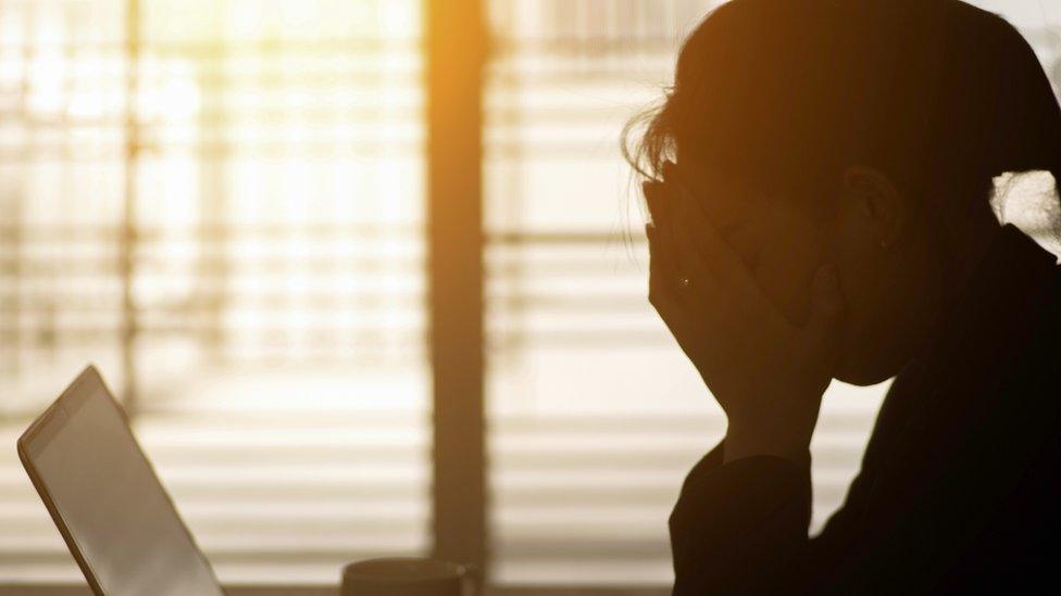 Stock anonymous image of a woman in shadow looking at her laptop.