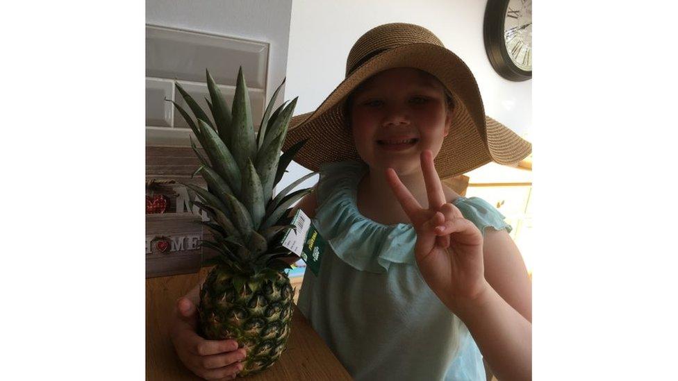 Girl wearing sunglasses poses with pineapple.