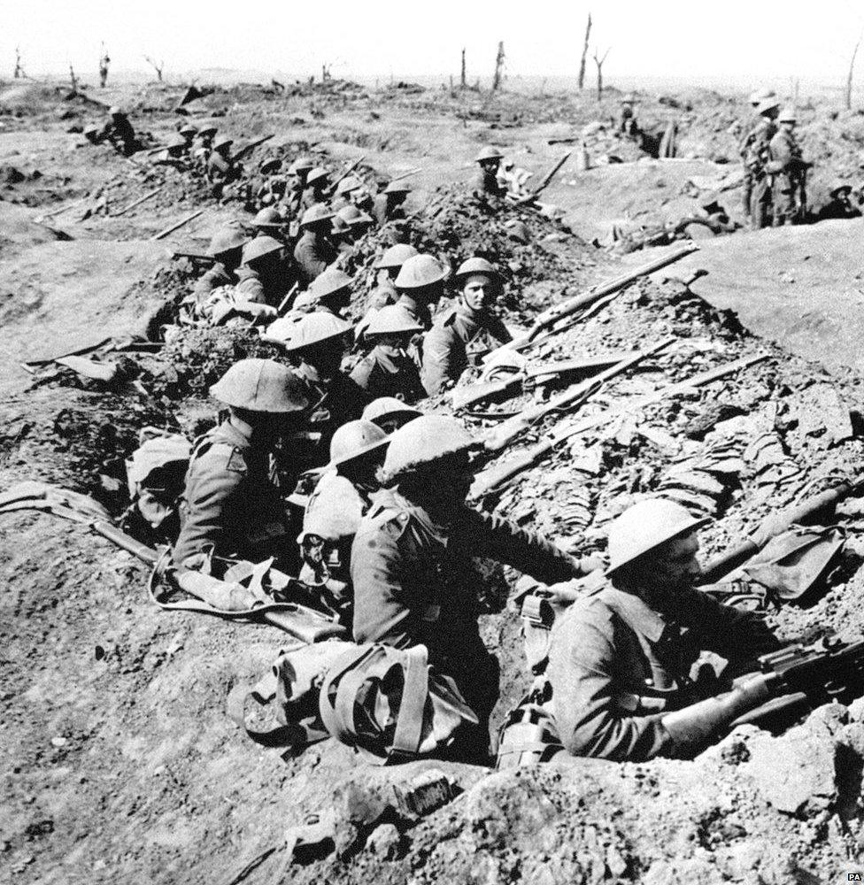 British infantrymen occupy a shallow trench in a ruined landscape before an advance during the Battle of the Somme