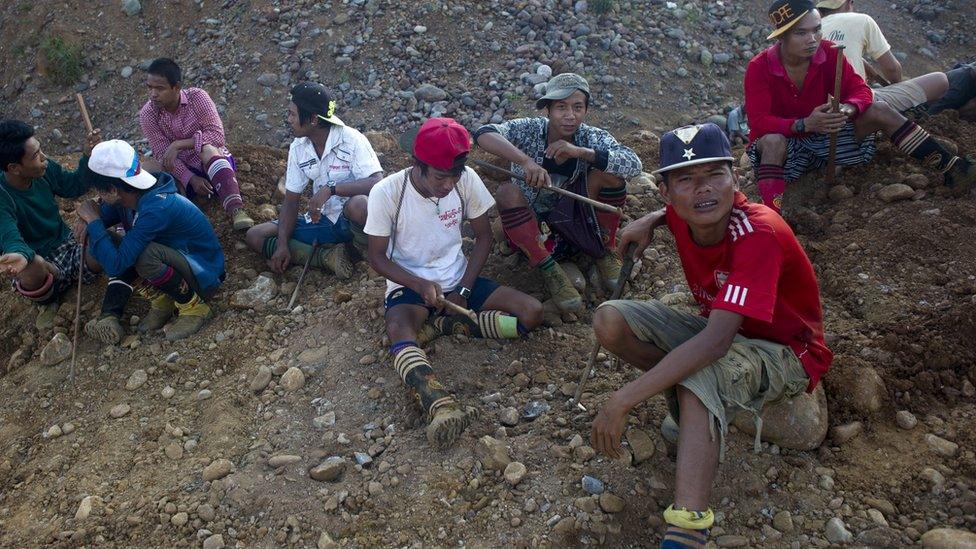 A group of men are sat in a pile of rubble, with hand held diggers