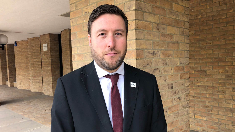 Pete Marland is shown standing wearing a suit with a shite shirt and a maroon tie outside Milton Keynes council offices