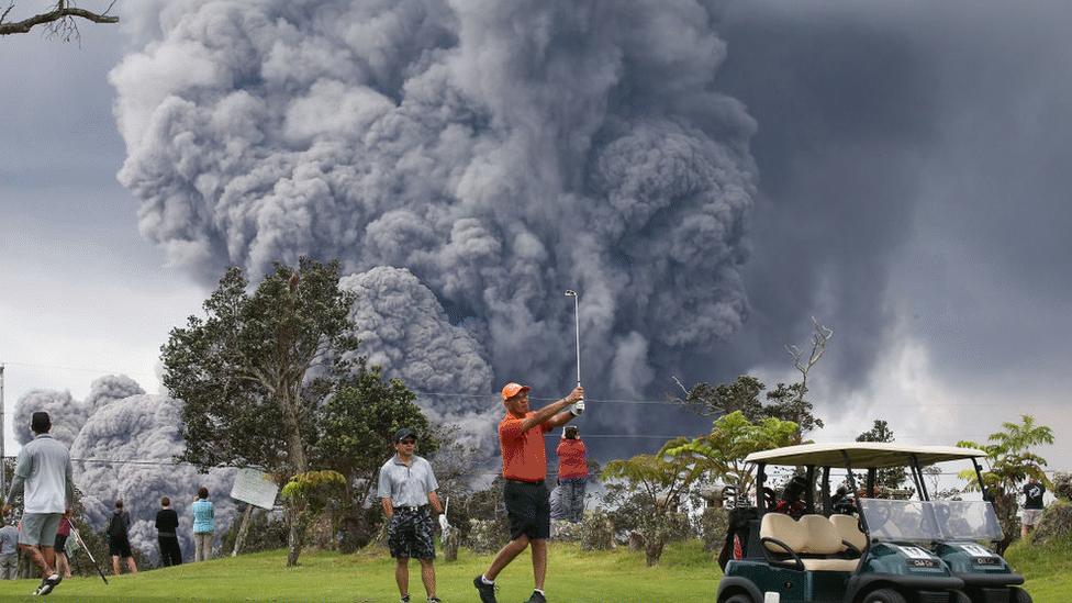 People-play-golf-as-an-ash-plume-rises-from-the-Kilauea-volcano.