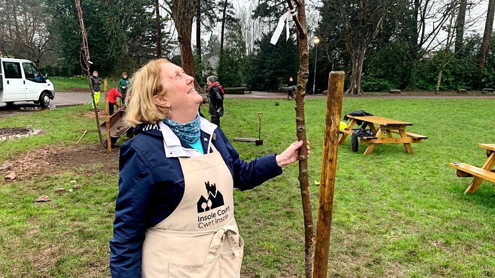 Trustee Valerie Mitchell holds a newly planted cherry tree