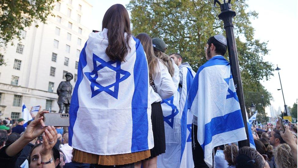 People wrapped in the Israeli flag take part in a vigil outside Downing Street