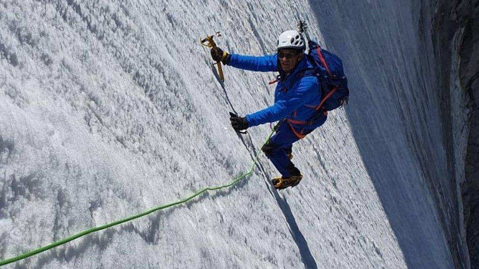 Eric Woerth climbing the almost vertical mountain peak, fully equipped with chisel, ropes and a helmet.