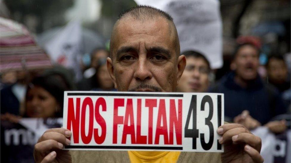 A man holds a sign that reads in Spanish: "We're missing 43" during a march marking the one year anniversary of the disappearances of 43 college students in Mexico City on 26 September 2015