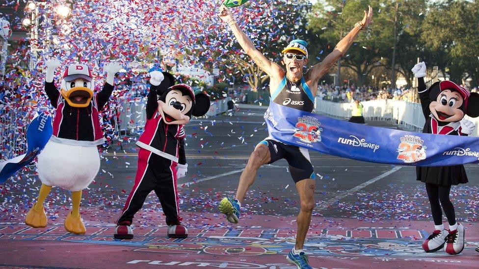 A-man-jumps-for-joy-next-to-Disney-characters-Donald-Duck-Mickey-and-Minnie-Mouse-as-he-finishes-the-Walt-Disney-World-Marathon.