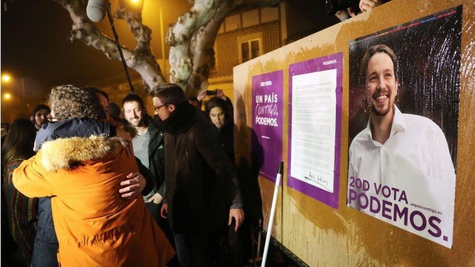 Podemos leader Pablo Iglesias hugs his father, Javier Iglesias, in front of a campaign poster for the general elections