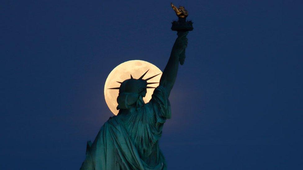 The Statue of Liberty in New York City, US, seen with the rising supermoon in the sky