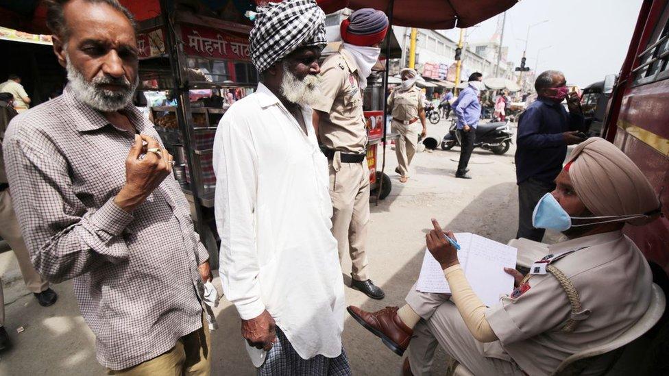 An Indian police officer (R), notes down details of defaulters who are not wearing face masks before testing them for Covid19 disease, in a mobile van set up to test random people who are not wearing the mandatory face masks, in Amritsar, India, 25 March 2021