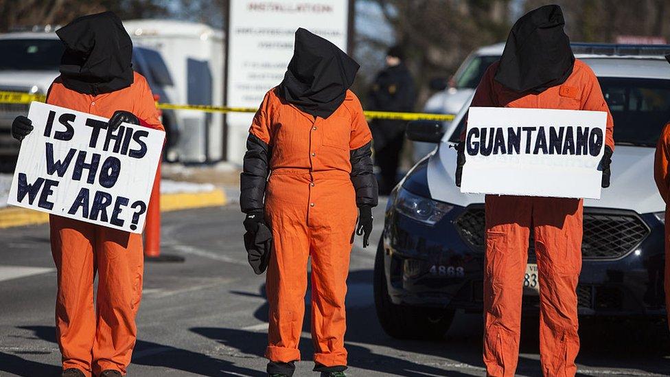 Activists holding 'Is this who we are' sign dressed as detainee