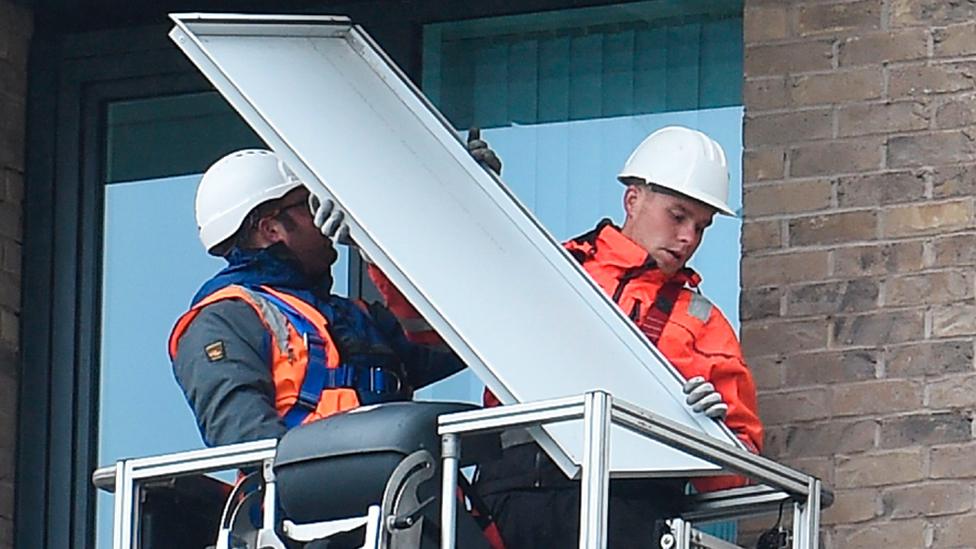 File picture of workers removing panels of external cladding from the facade of a building in Manchester