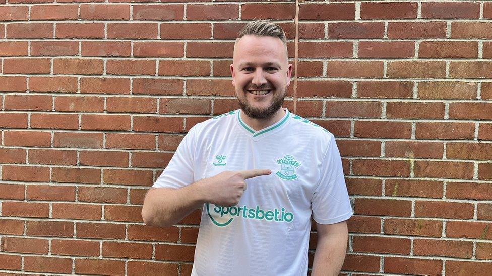 Dan Hiscock, in his white Southampton replica shirt, in front of a brick wall