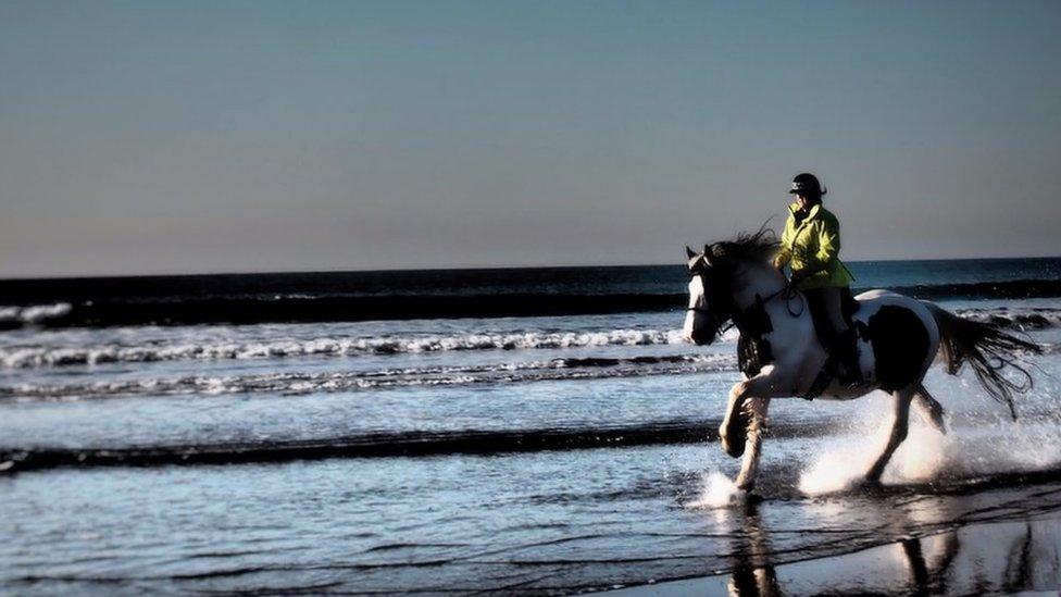 Horse rider gallops through sea at Dinas Dinlle beach, Gwynedd