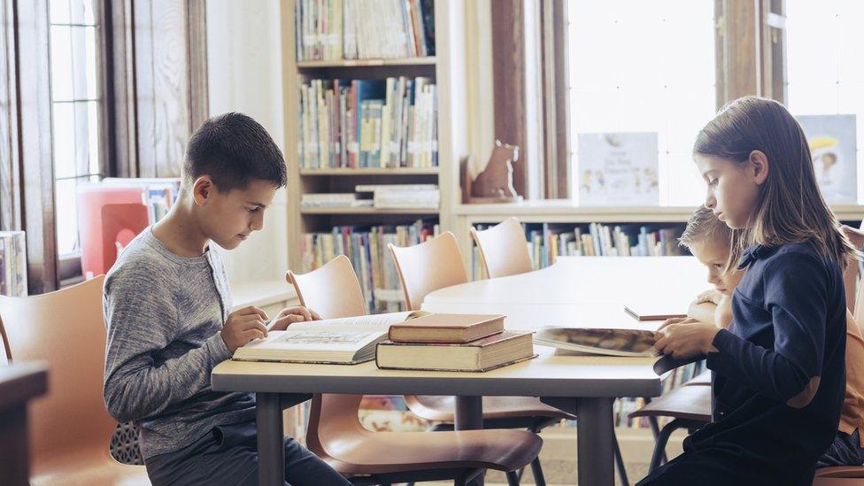 Three children reading, surrounded by books