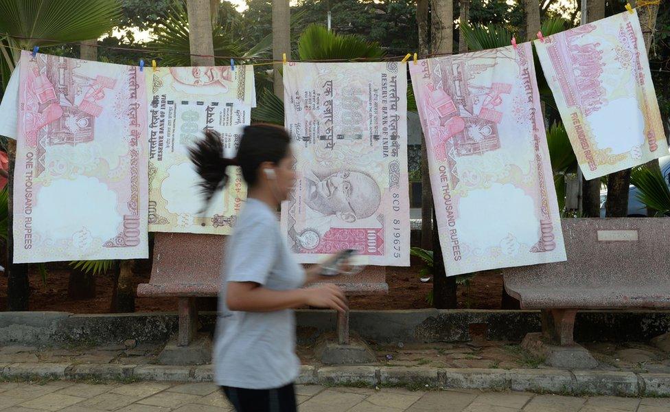 A jogger passes replica prints of discontinued 500 and 1000 rupee notes as part of a street art exhibition in Mumbai