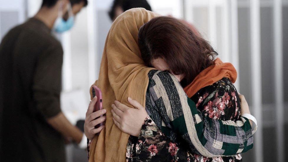 A woman embraces her sister-in-law as she arrives with other Afghan refugees