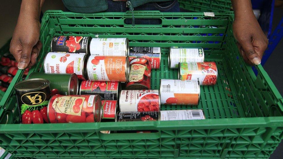 A man holds a tray containing tins of food