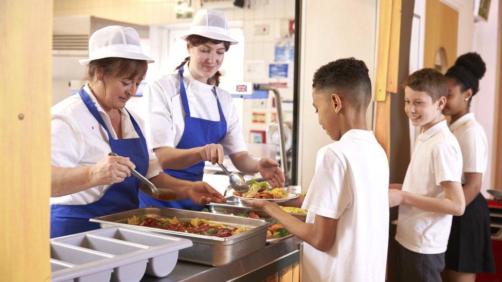 Two school dinner staff serve lunches to children