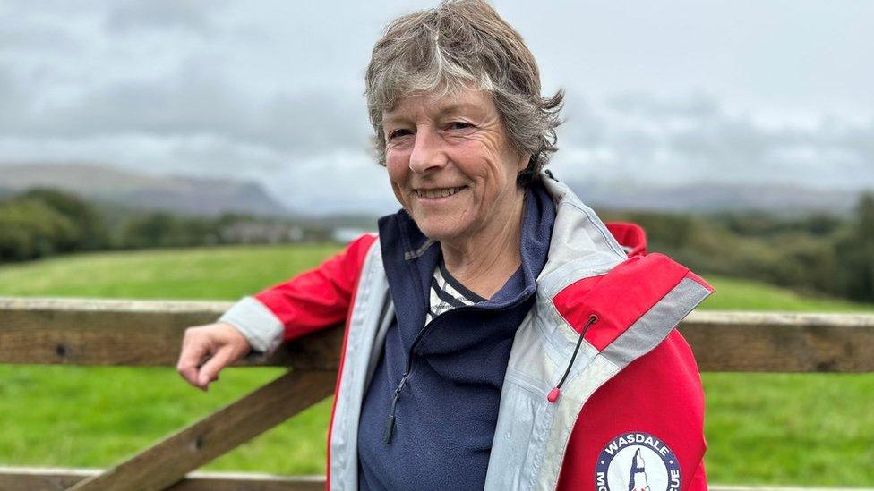 A woman in a red mountain rescue jacket smiles at the camera