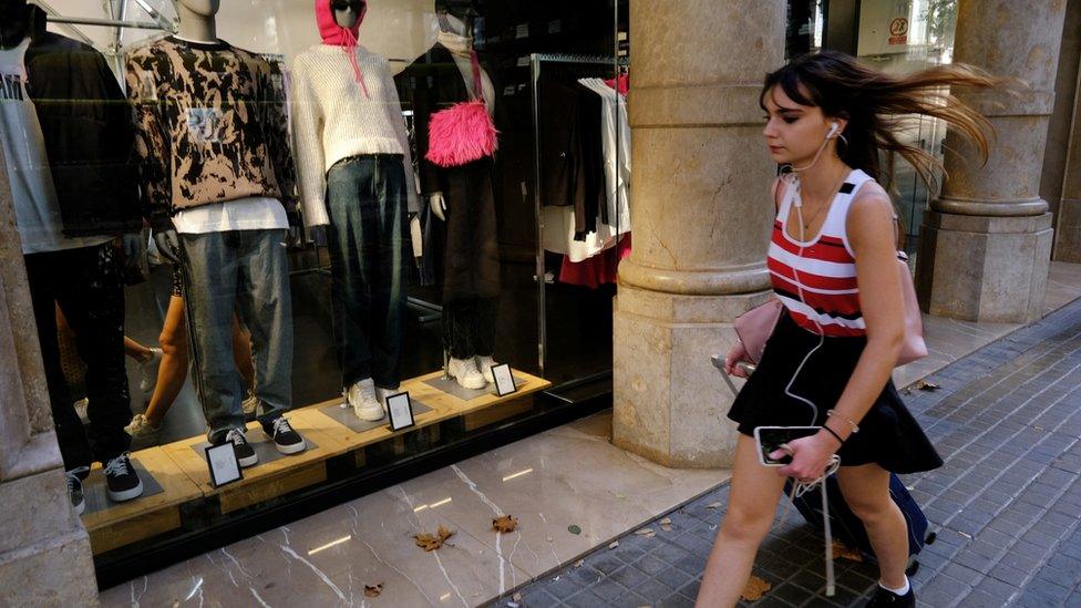 A tourist walks past a shopping window with mannequins dressed with warm clothing amid hot weather in Barcelona, Spain, 27 October