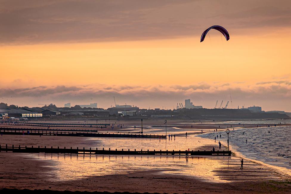 Winding Down Flying High - a beach with distant figures of people under an orange sky