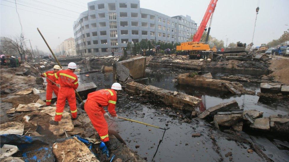 Emergency services personnel standing next to a large pool of oil and rubble