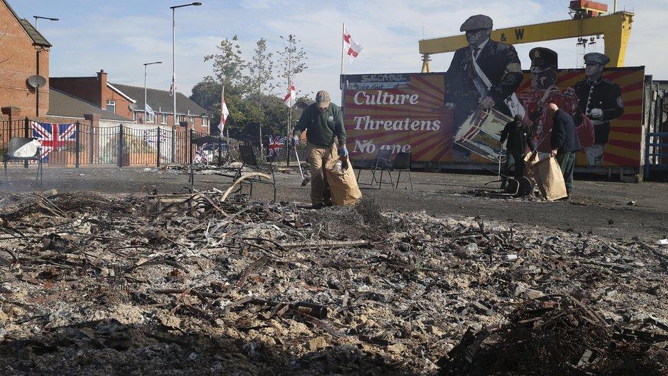 People clearing up after a bonfire on the Newtownards Road