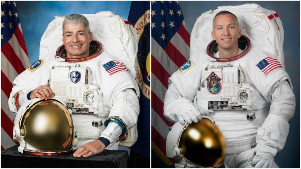 Two astronauts in space suits sit by the USA flag.