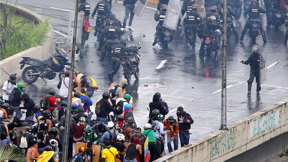 A member of the riot security forces points what appears to be a pistol towards a crowd of demonstrators during a rally against Venezuela's President Nicolas Maduro's government in Caracas, 19 June