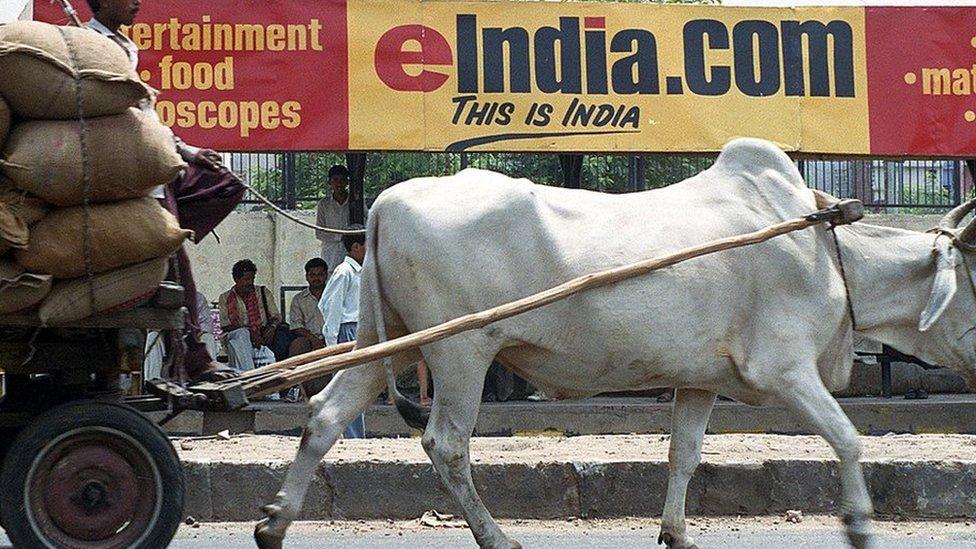 A bullock-driven cart rides past a bus stop billboard advertising one of India's many internet portals 01 June 2000 in New Delhi.