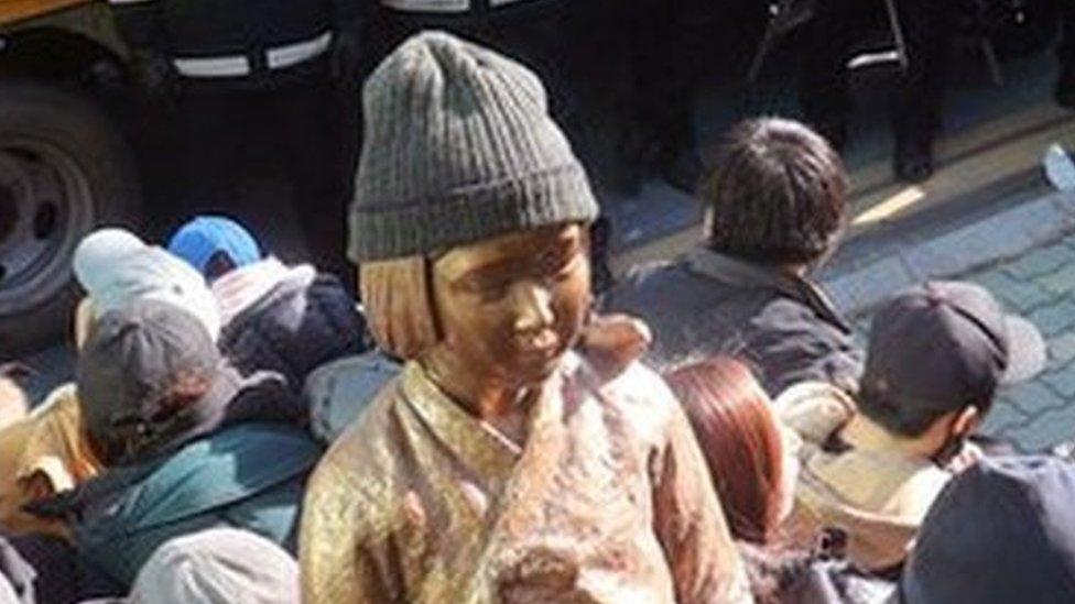 In this 28 December 2016, photo, members of civic groups sit around a comfort-woman statue after they set up in front of the Japanese consulate as police officers surround them in Busan, South Korea.