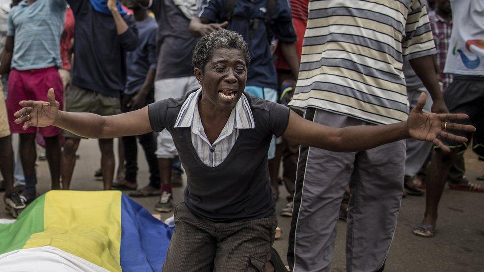A woman cries over the body of Axel Messa, 30, wrapped in the flag of Gabon after he was shot in front of his home, 2 September 2016