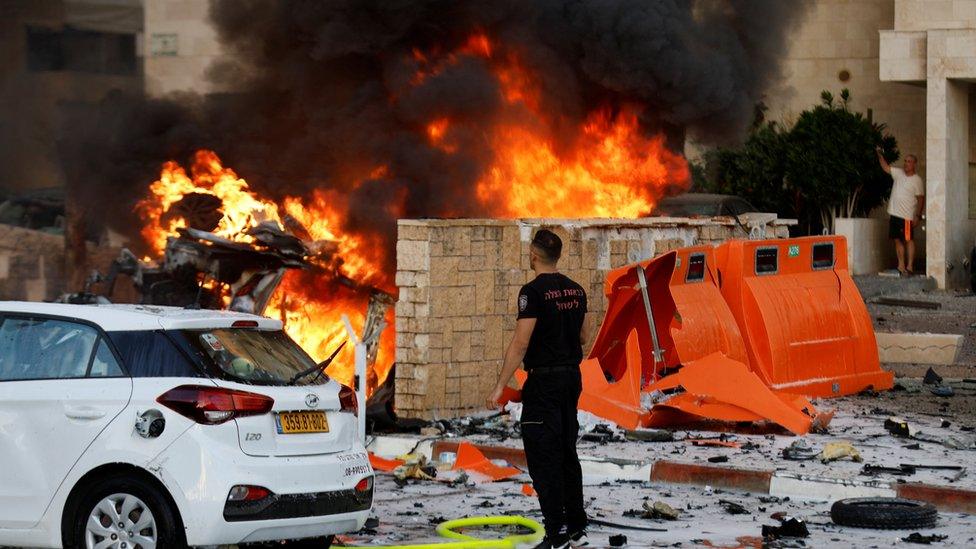 A man stands on a road as fire burns after rockets were launched from the Gaza Strip, in Ashkelon, Israel