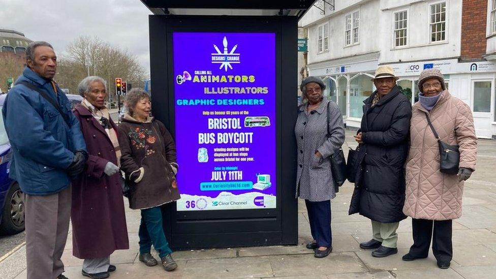 Six people standing next to the bus stop which has a poster advertising the Bristol bus boycott competition