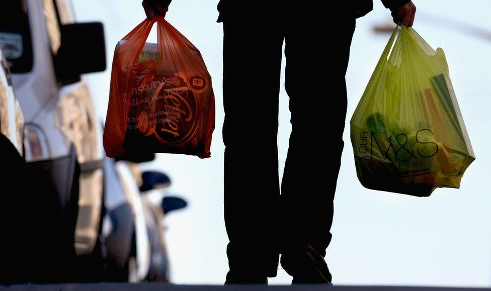 Man carries two plastic bags down road