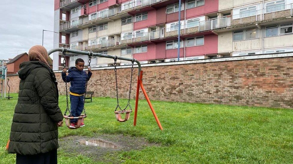 Muna Hussein and Maahir outside a housing block, playing on swings.