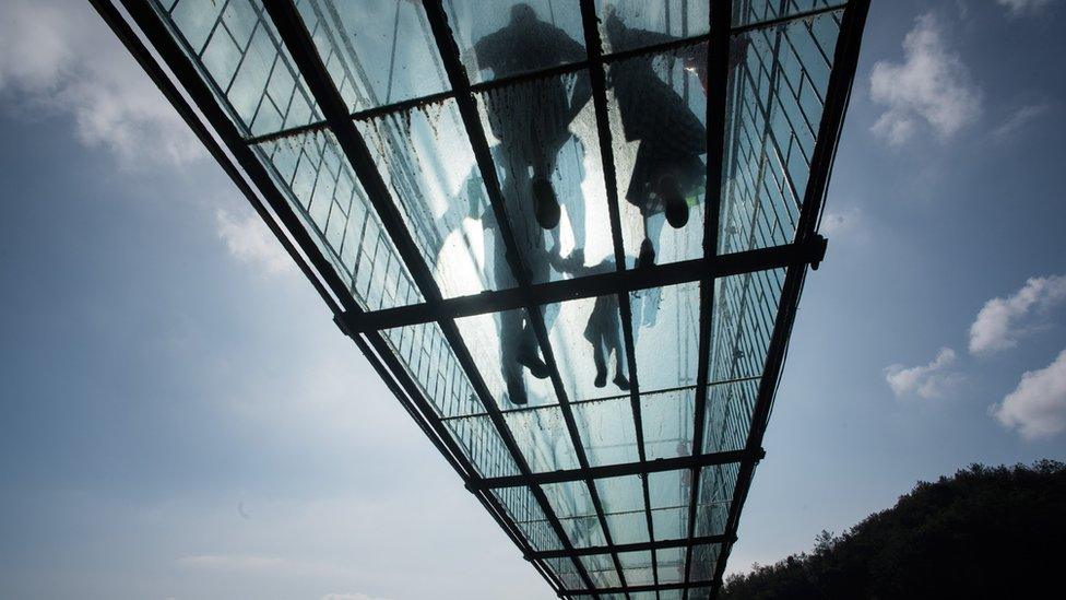 Chinese tourists walk across a glass-bottomed suspension bridge in the Shiniuzhai mountains in Pingjiang county, Hunan province