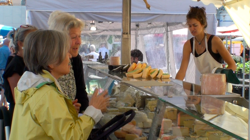 A busy cheese stall at a farmers' market is perused by several ladies