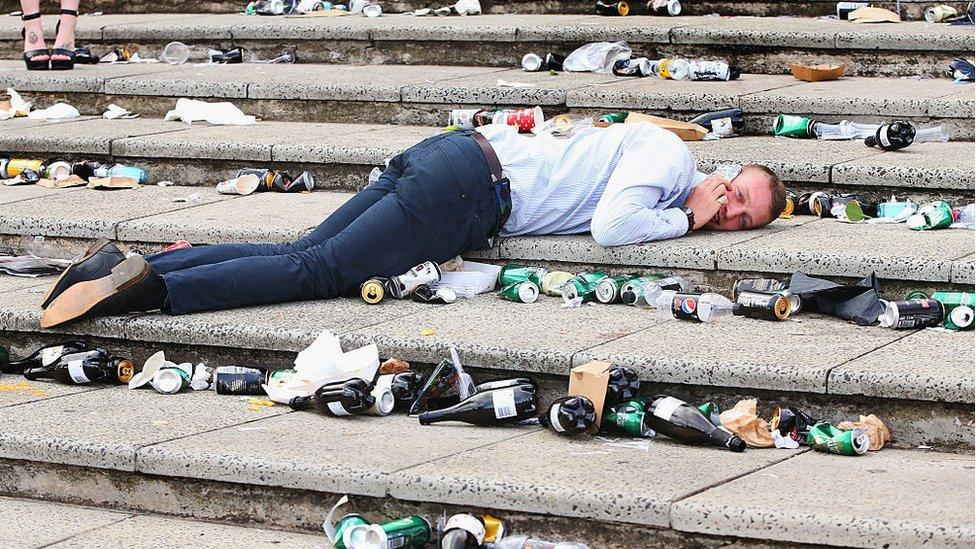 A man lies on the ground amid beer cans while talking on the phone