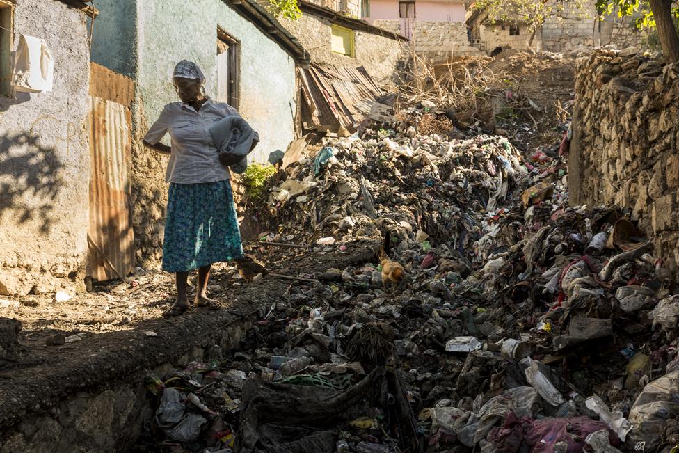 A woman stands in front of rubbish washed down the mountain