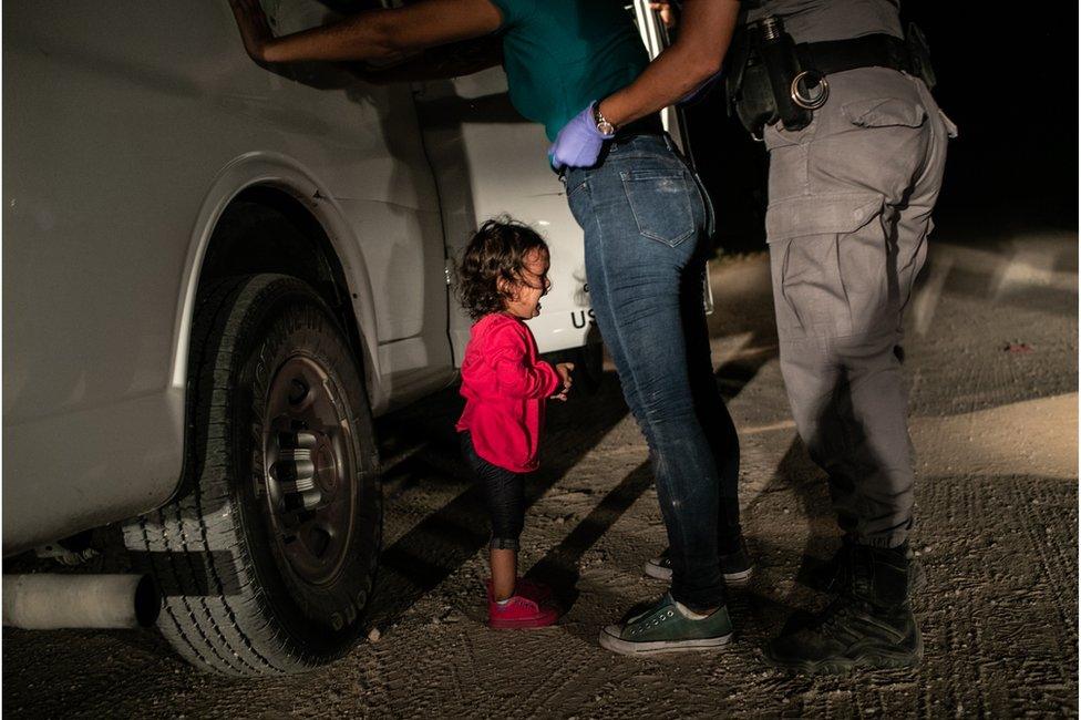 A child cries as two adults stand nearby