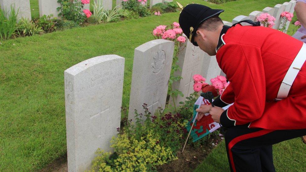 A member of the band of the Royal Welsh lays a flag at the grave of a Welsh soldier at Flatiron Copse cemetery