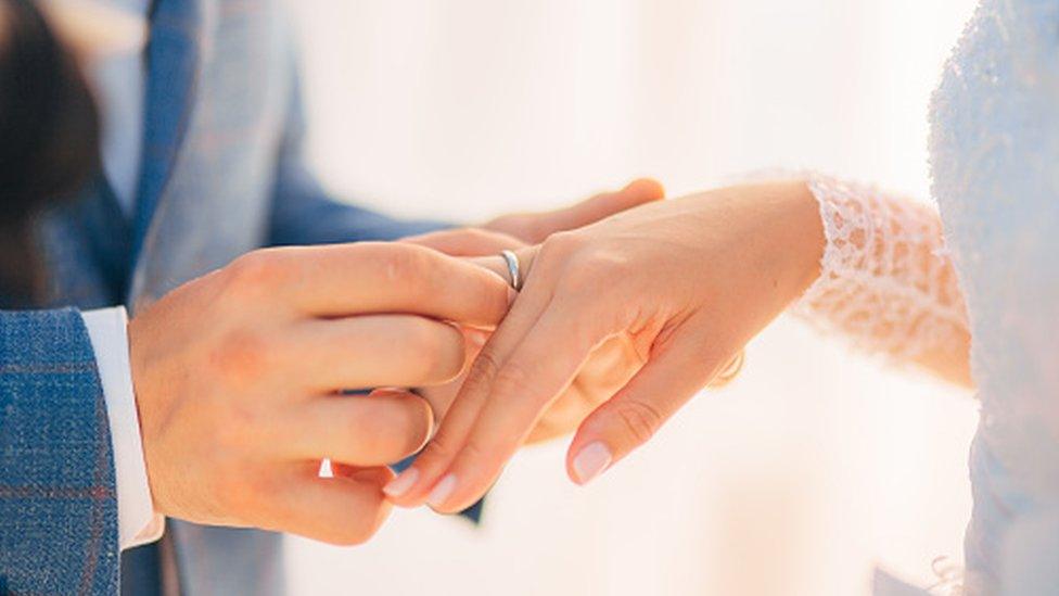 A groom puts a ring on a bride's finger